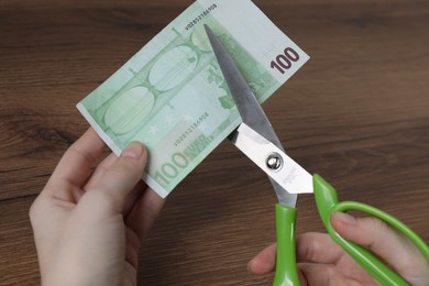 Photo of Woman cutting euro banknote at wooden table, closeup