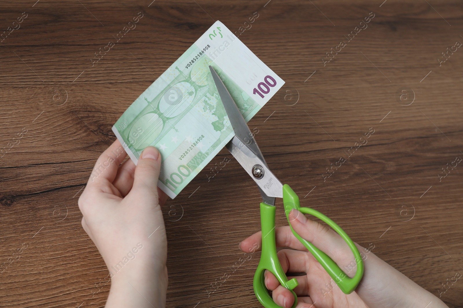 Photo of Woman cutting euro banknote at wooden table, top view