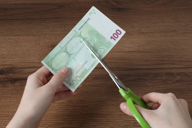 Photo of Woman cutting euro banknote at wooden table, top view