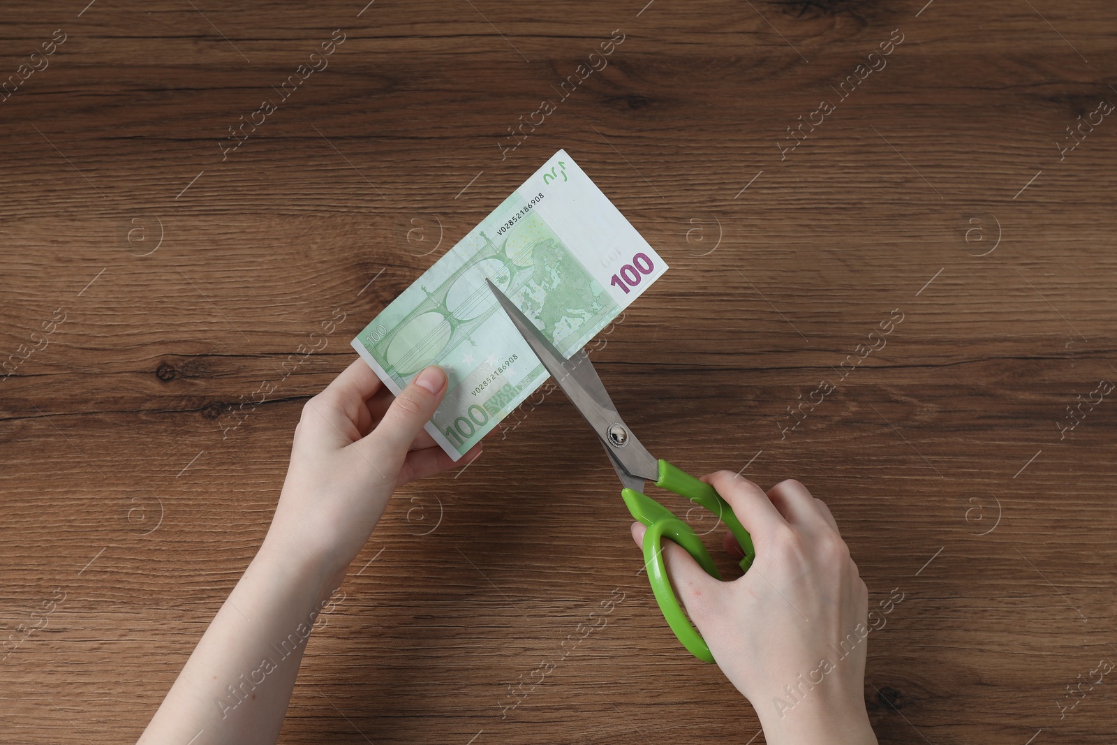 Photo of Woman cutting euro banknote at wooden table, top view