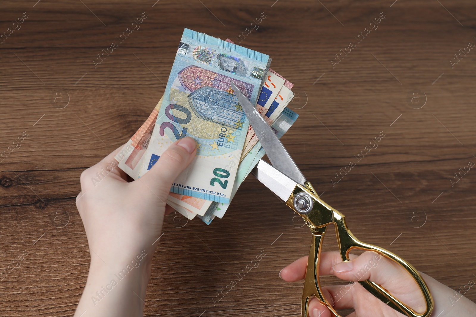 Photo of Woman cutting euro banknotes at wooden table, closeup