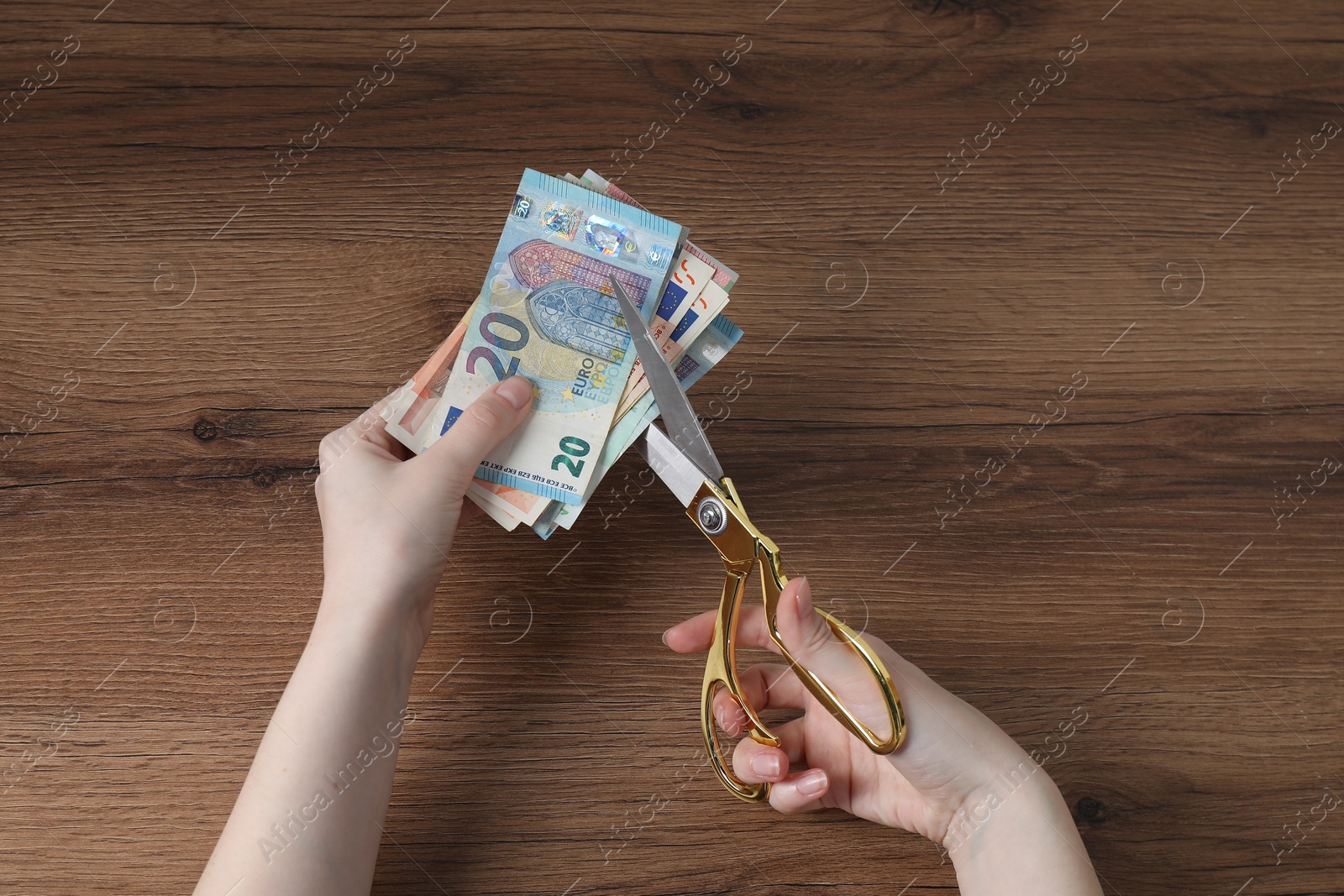 Photo of Woman cutting euro banknotes at wooden table, top view