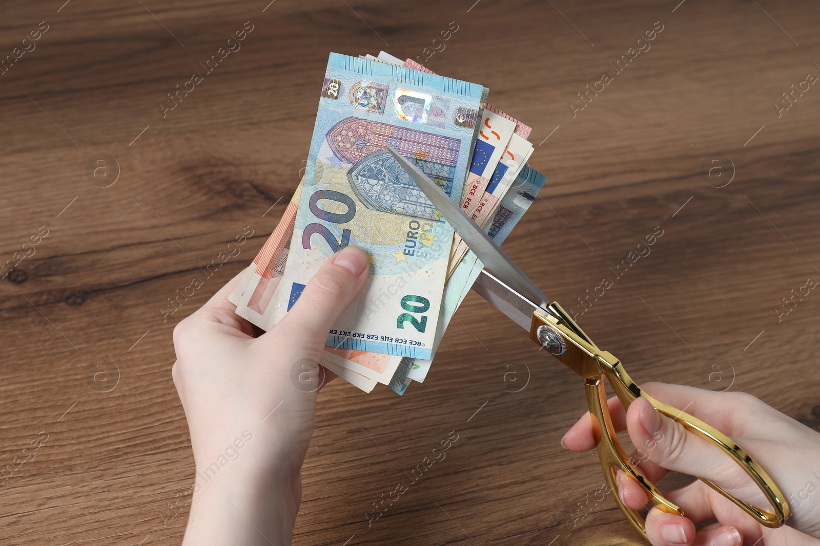 Photo of Woman cutting euro banknotes at wooden table, closeup