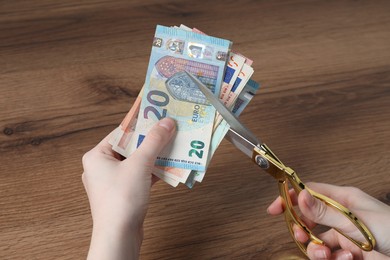 Photo of Woman cutting euro banknotes at wooden table, closeup