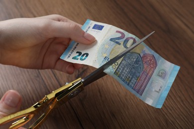 Photo of Woman cutting euro banknote at wooden table, closeup