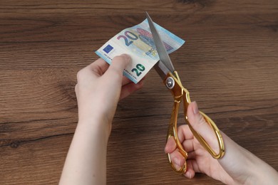 Photo of Woman cutting euro banknote at wooden table, closeup