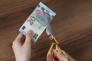 Photo of Woman cutting euro banknote at wooden table, closeup