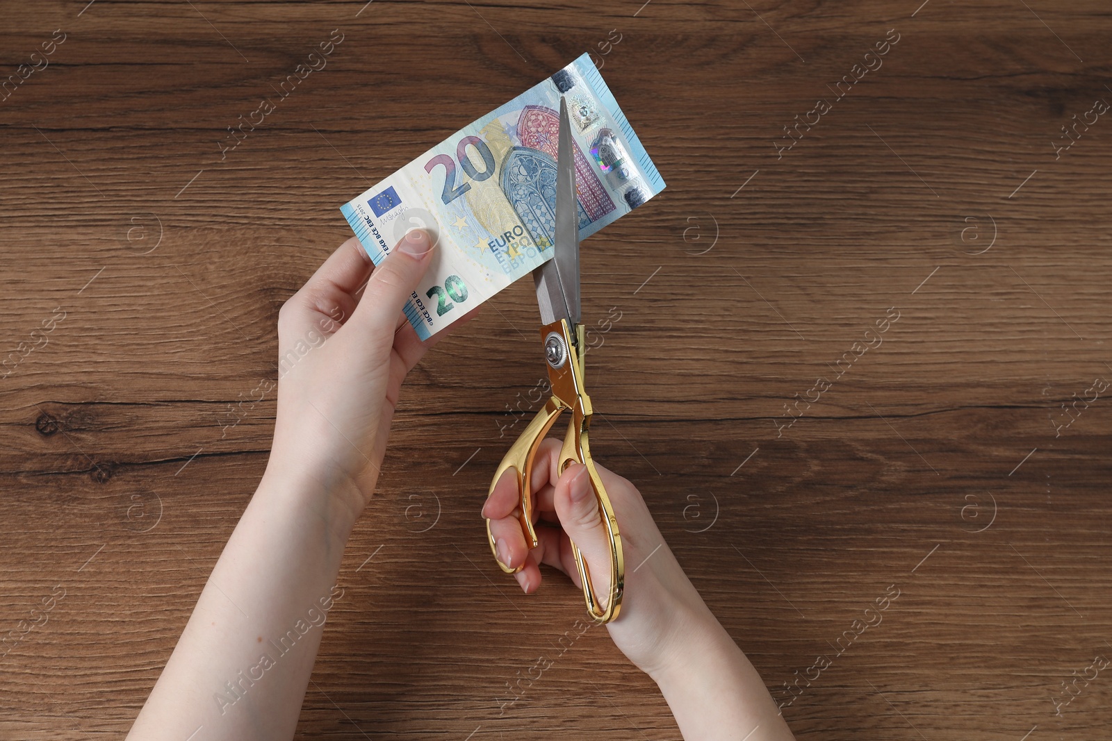 Photo of Woman cutting euro banknote at wooden table, top view