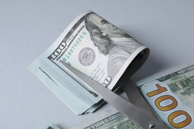 Photo of Dollar banknotes and scissors on gray background, closeup