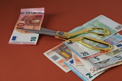 Photo of Euro banknotes and scissors on brown background, closeup