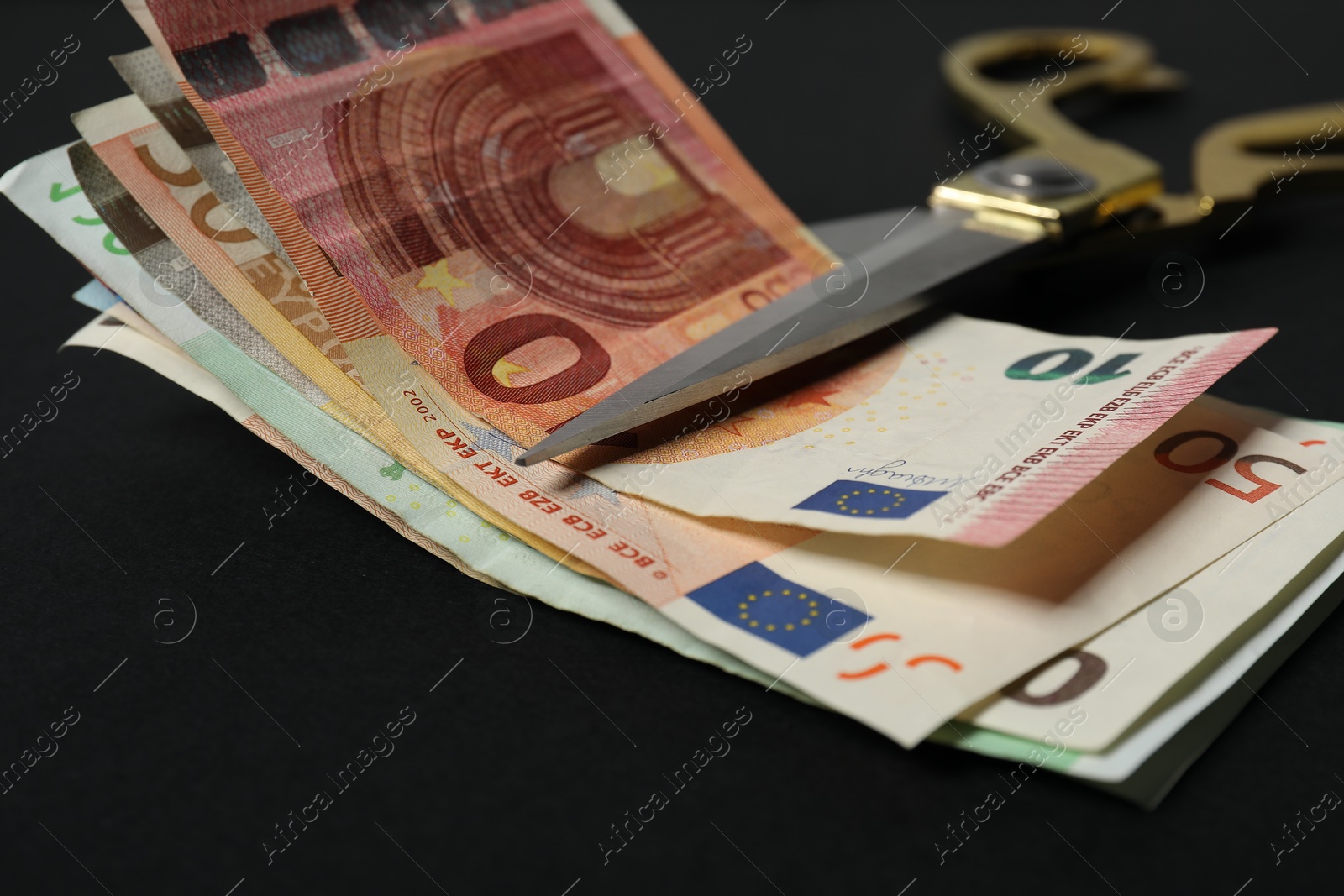 Photo of Euro banknotes and scissors on black background, closeup