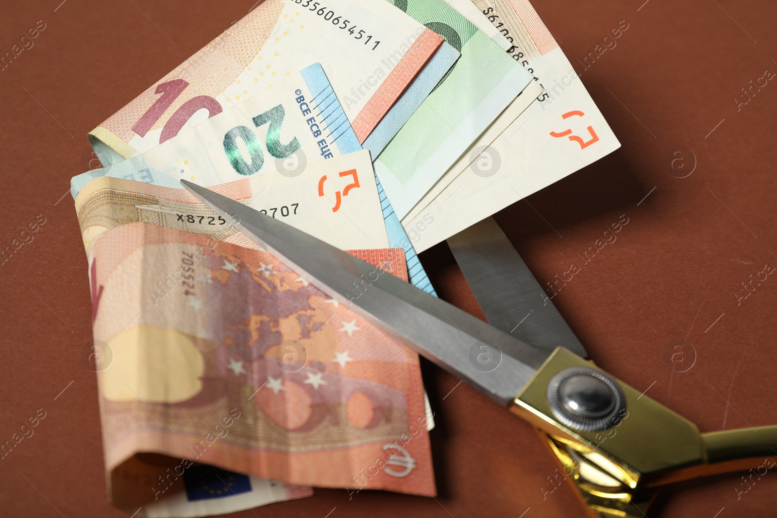 Photo of Euro banknotes and scissors on brown background, closeup