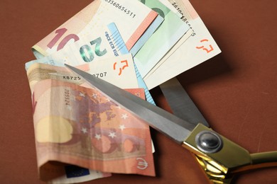 Photo of Euro banknotes and scissors on brown background, closeup