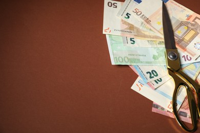 Photo of Euro banknotes and scissors on brown background, space for text