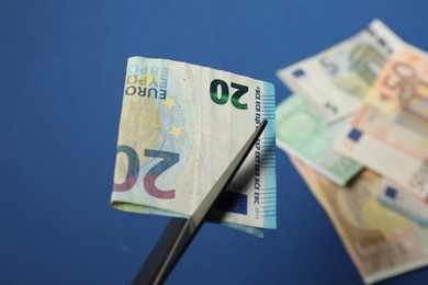 Photo of Scissors and euro banknote on blue background, selective focus