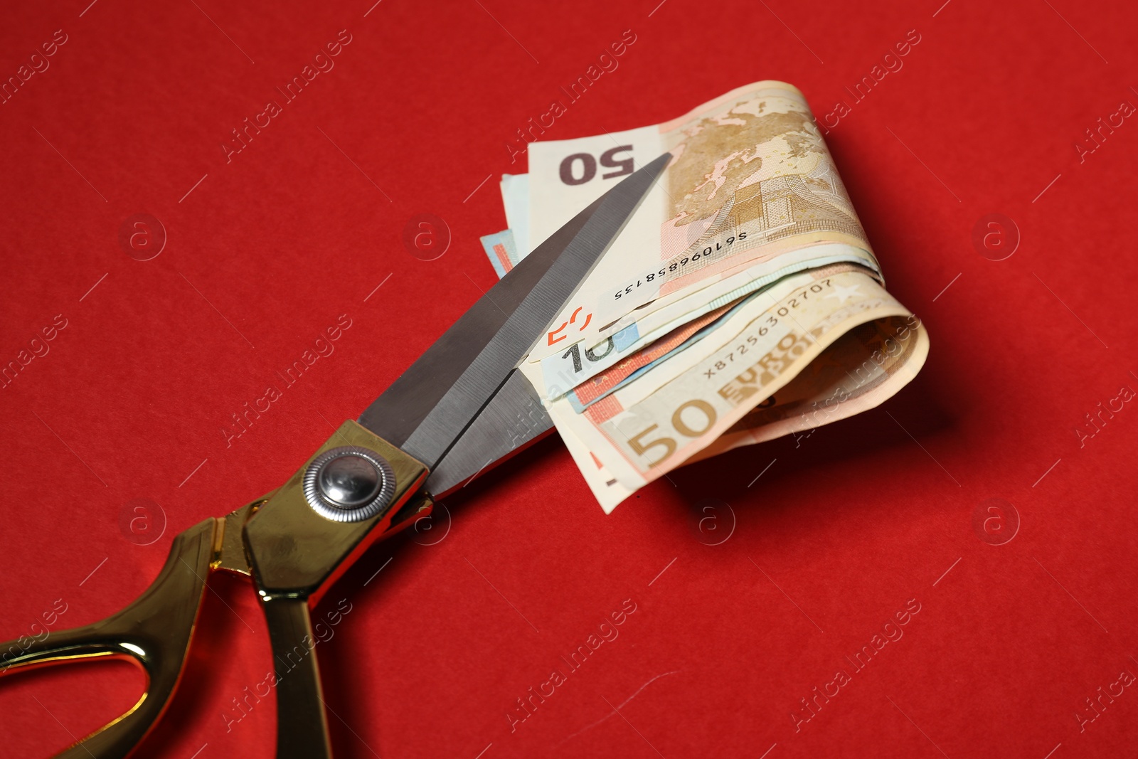 Photo of Euro banknotes and scissors on red background, closeup