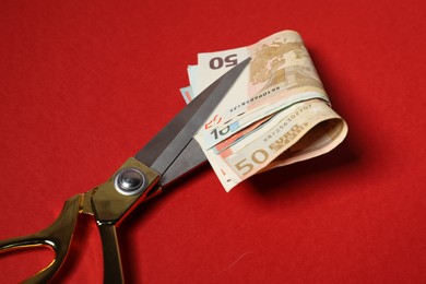 Photo of Euro banknotes and scissors on red background, closeup