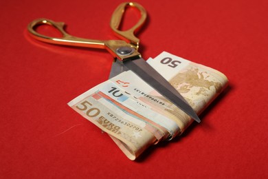 Photo of Euro banknotes and scissors on red background, closeup