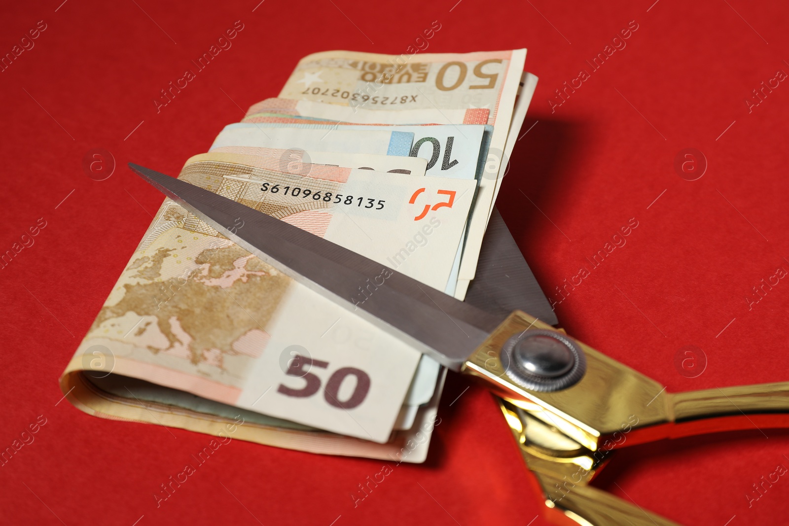 Photo of Euro banknotes and scissors on red background, closeup