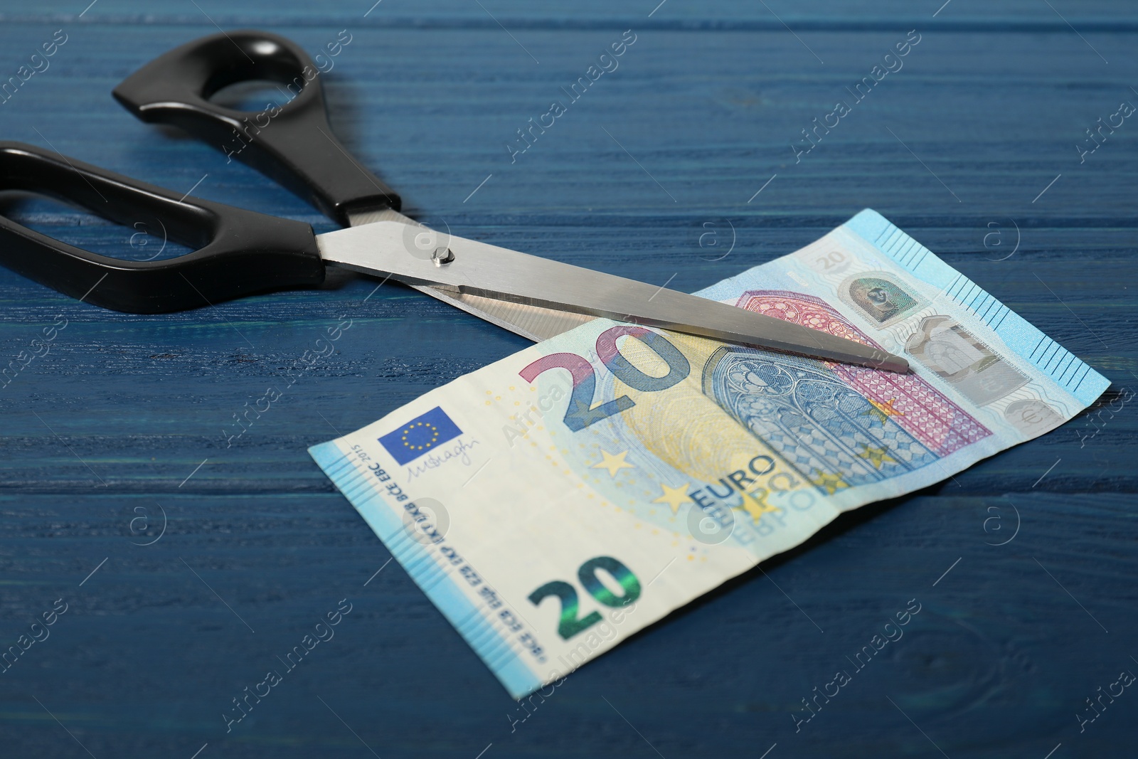 Photo of Scissors with euro banknote on blue wooden table, closeup