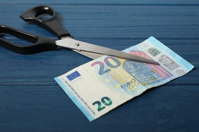 Photo of Scissors with euro banknote on blue wooden table, closeup