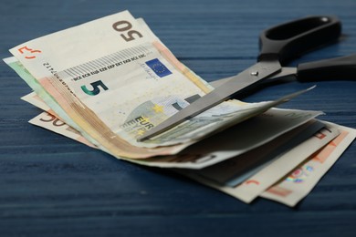 Photo of Euro banknotes and scissors on blue wooden table, closeup