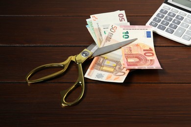 Photo of Euro banknotes, scissors and calculator on wooden table