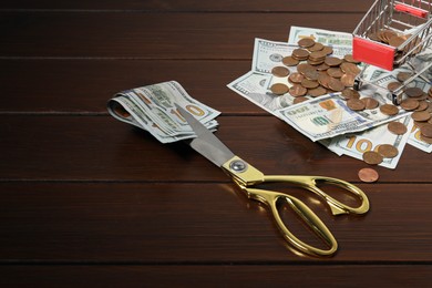 Photo of Dollar banknotes, scissors, coins and small shopping cart on wooden table