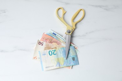 Photo of Euro banknotes and scissors on light marble table, top view