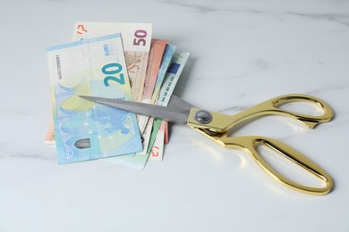 Photo of Euro banknotes and scissors on light marble table