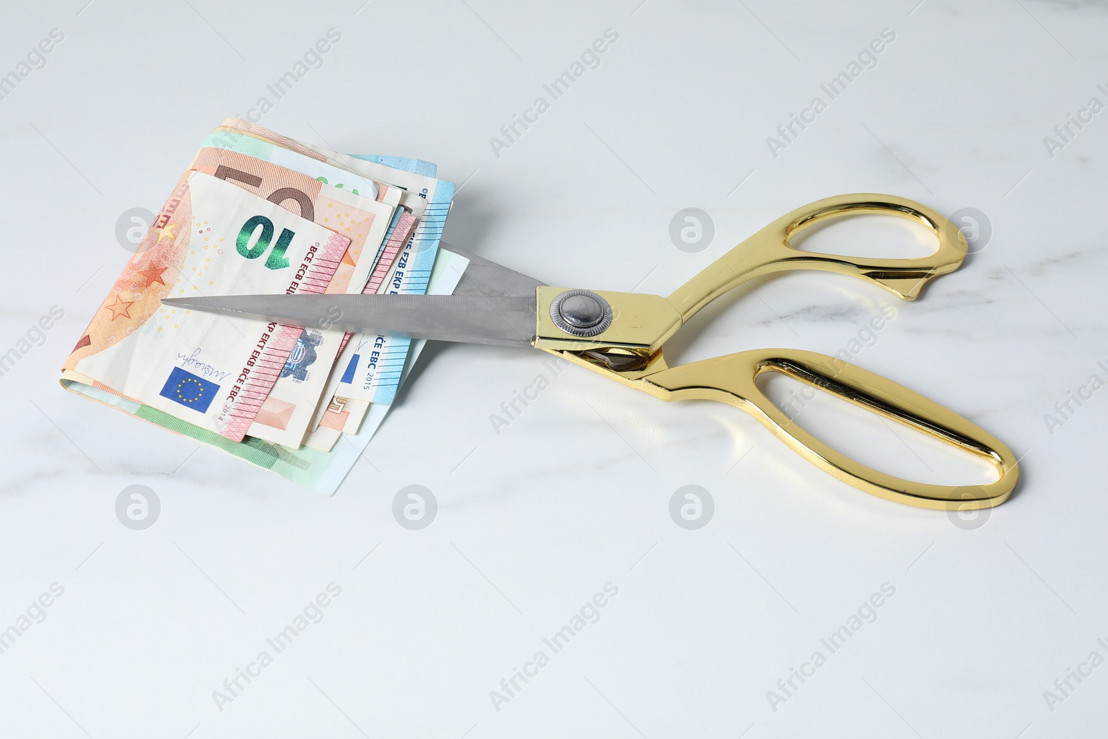 Photo of Euro banknotes and scissors on light marble table