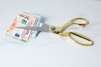 Photo of Euro banknotes and scissors on light marble table