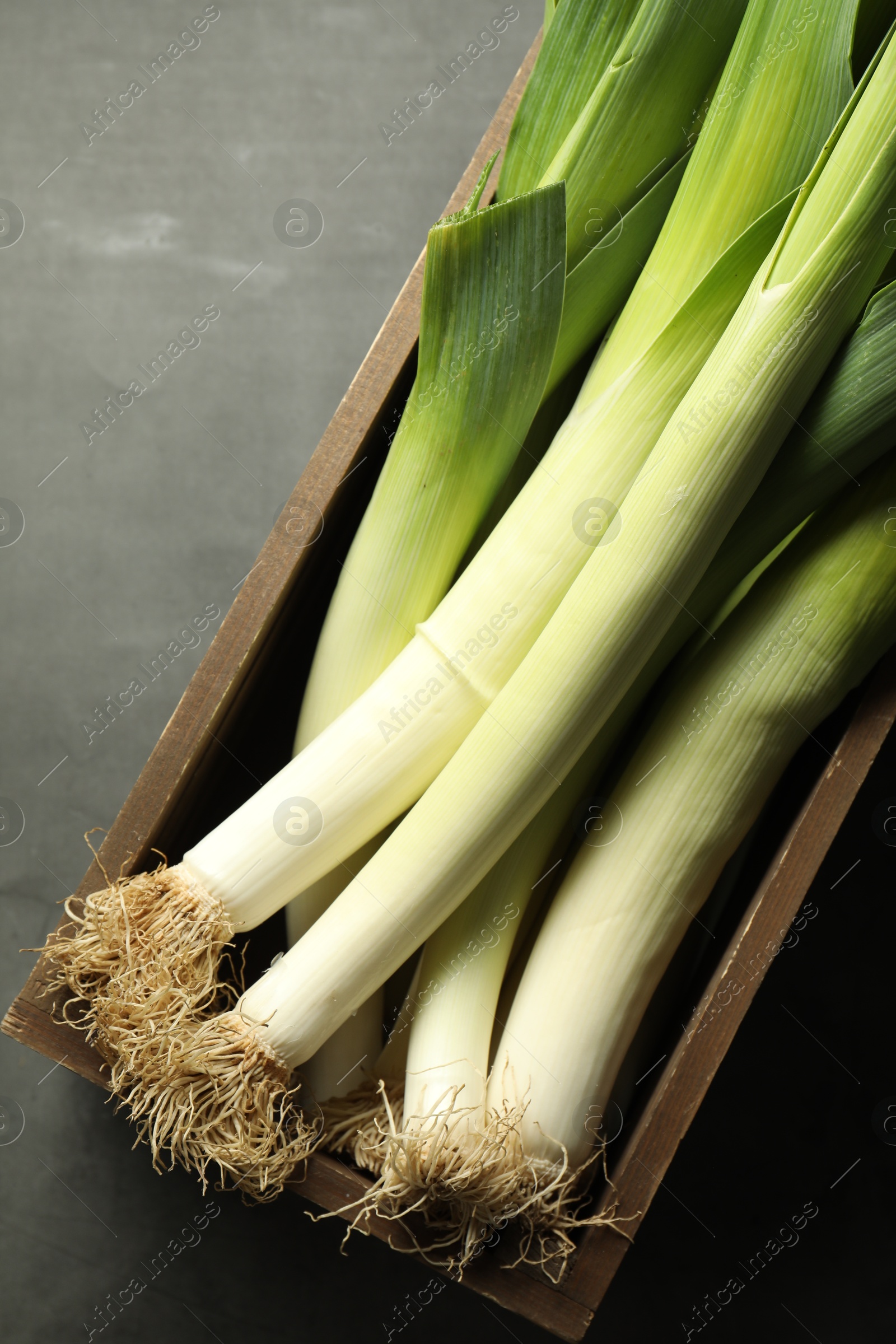 Photo of Fresh raw leeks in wooden crate on grey table, top view