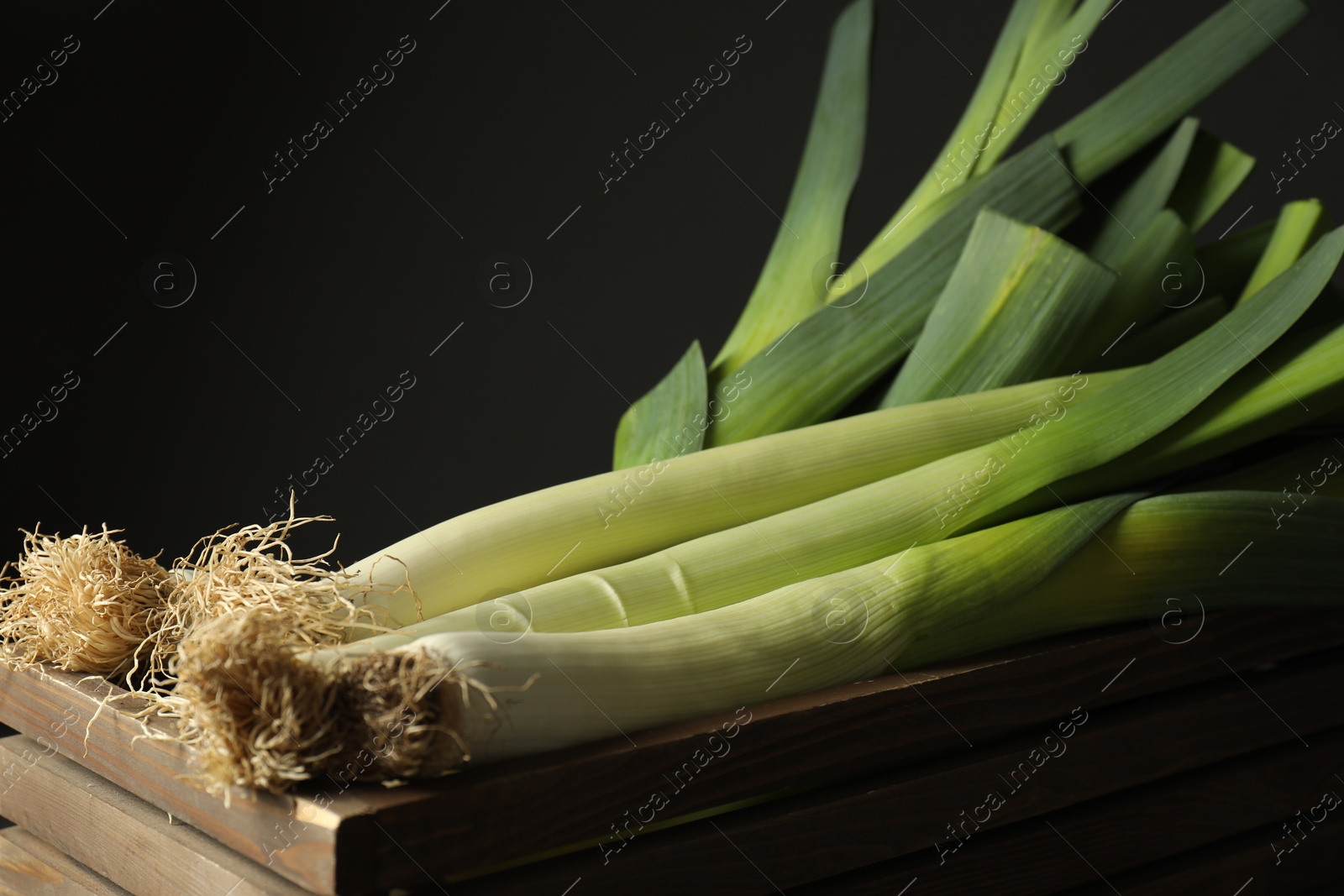 Photo of Fresh raw leeks in wooden crate on black background, closeup