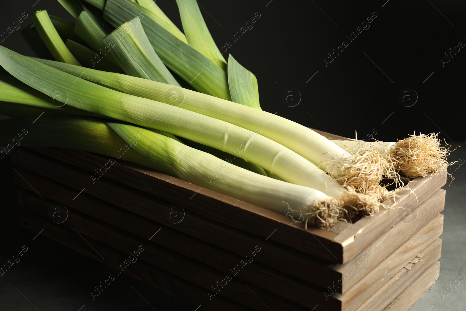 Photo of Fresh raw leeks in wooden crate on grey table, closeup