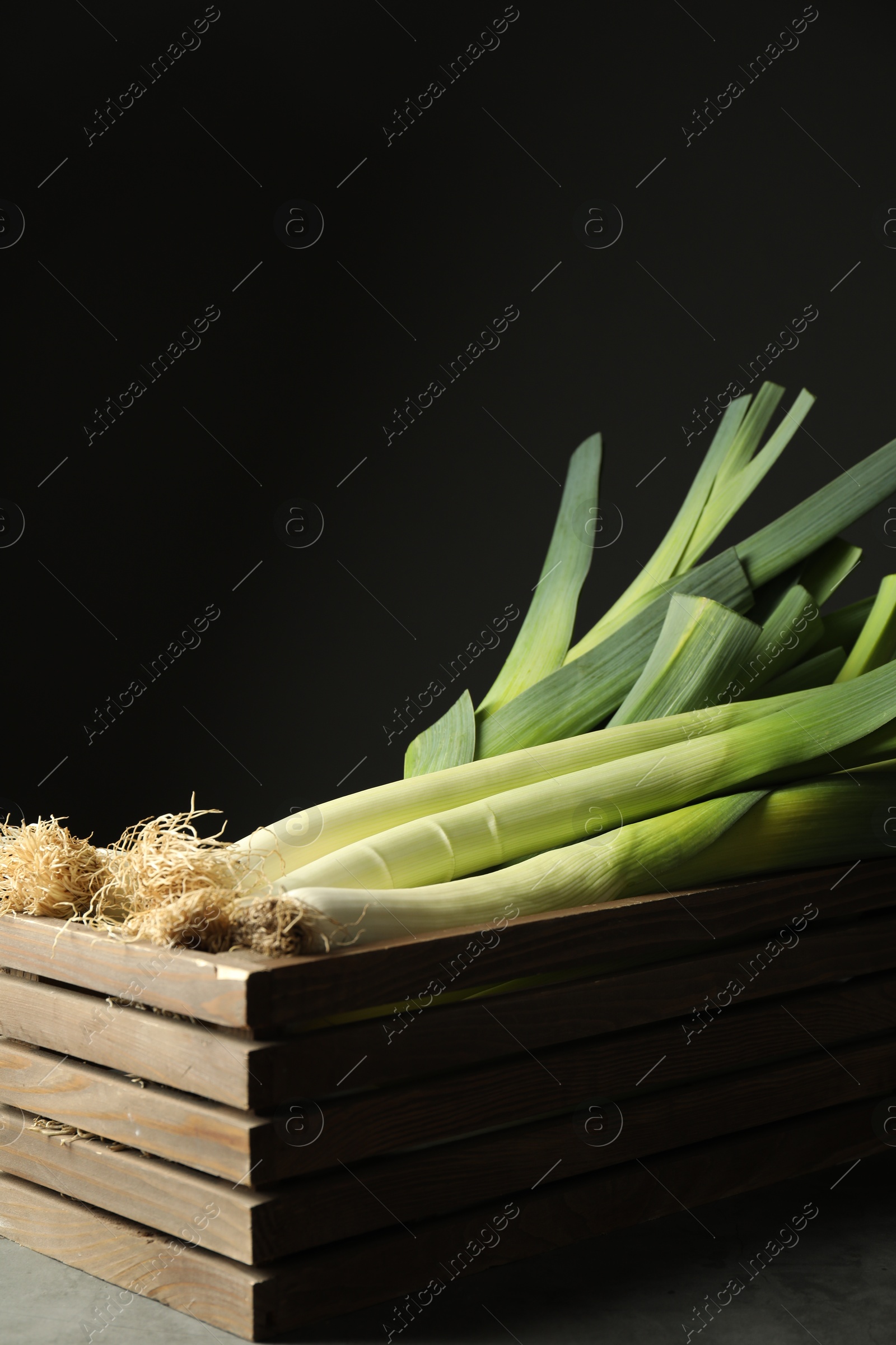 Photo of Fresh raw leeks in wooden crate on grey table, closeup