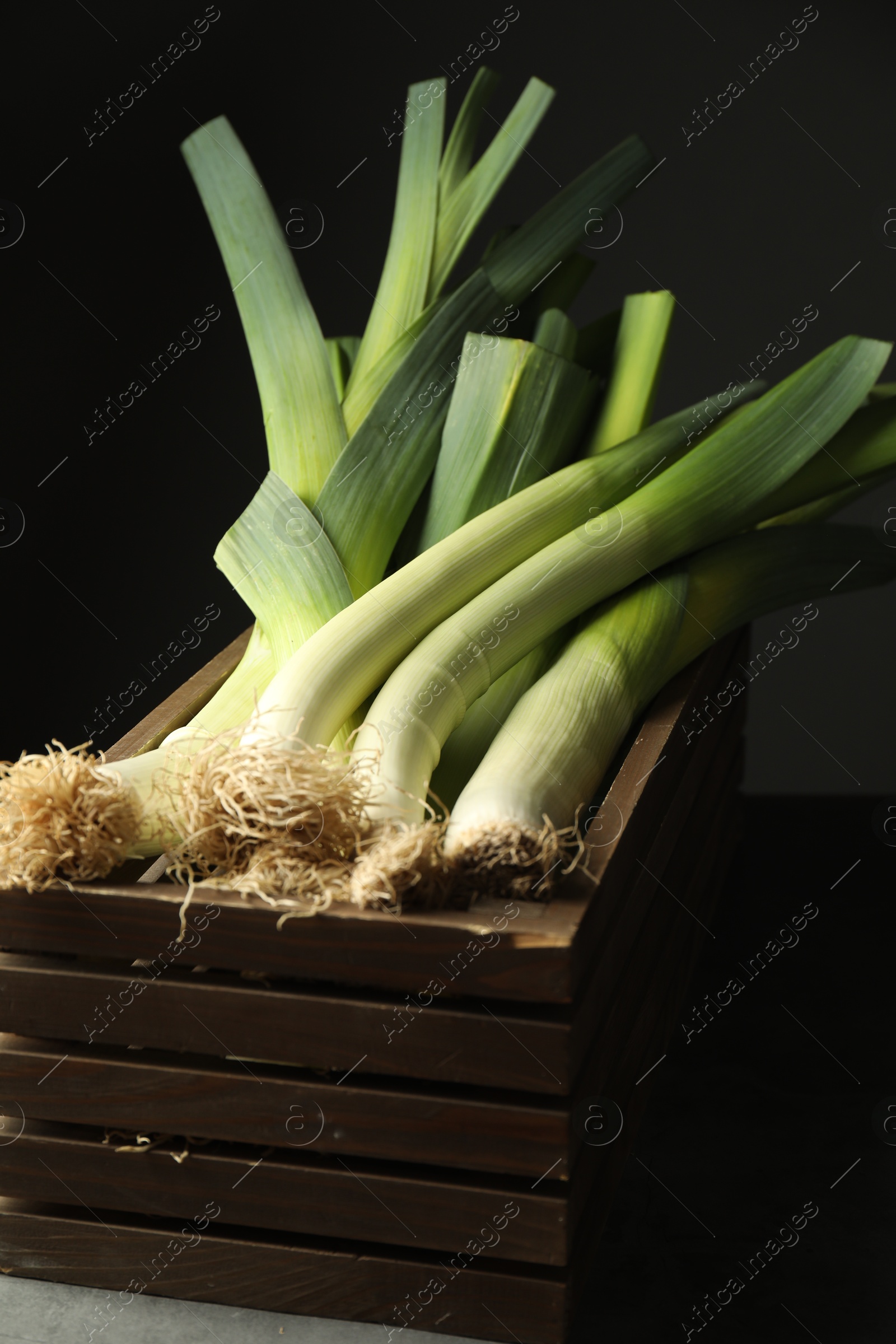 Photo of Fresh raw leeks in wooden crate on grey table, closeup