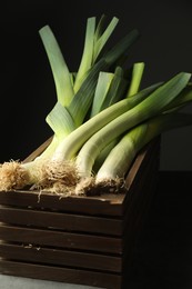 Photo of Fresh raw leeks in wooden crate on grey table, closeup