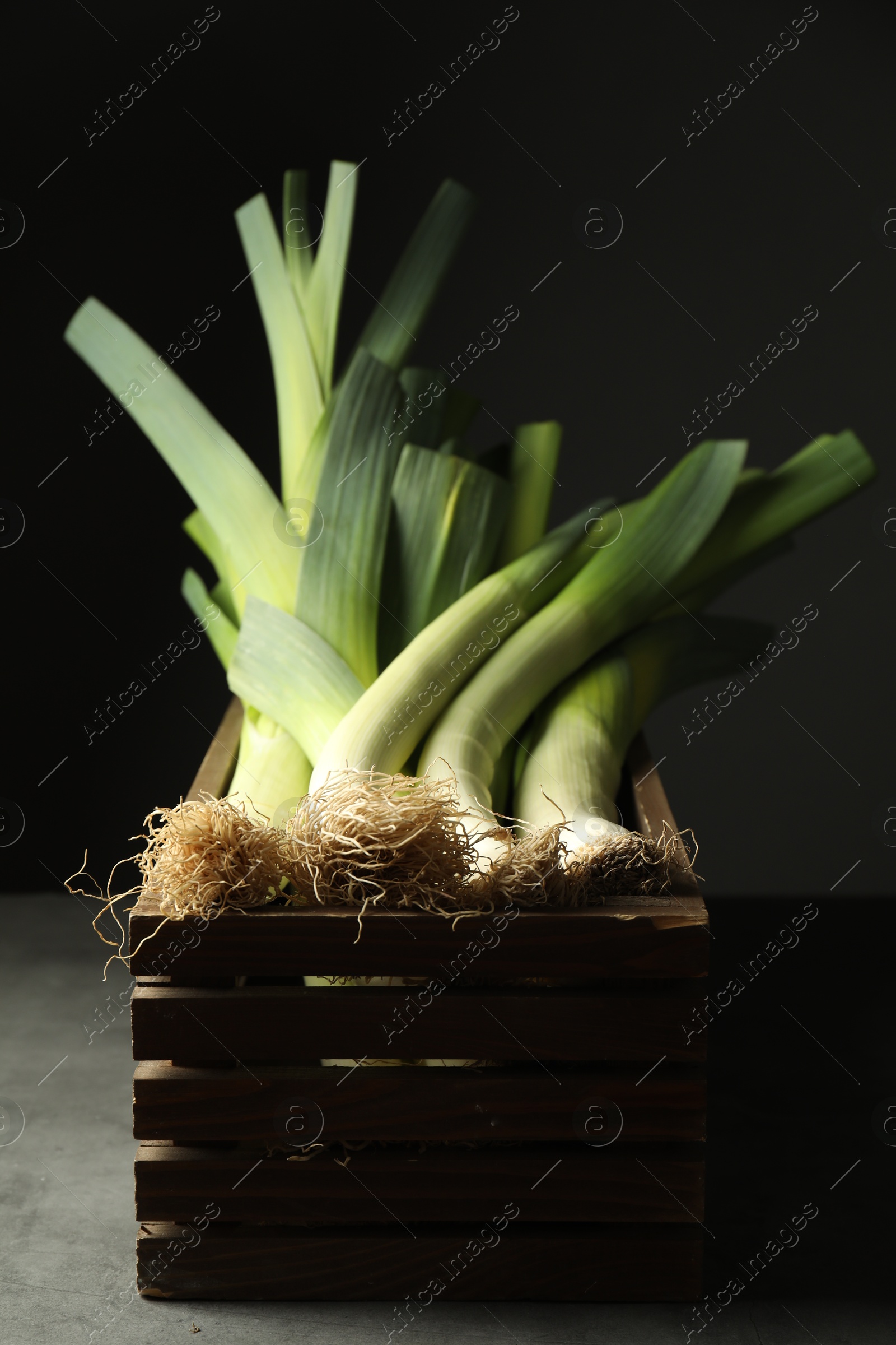 Photo of Fresh raw leeks in wooden crate on grey table, closeup