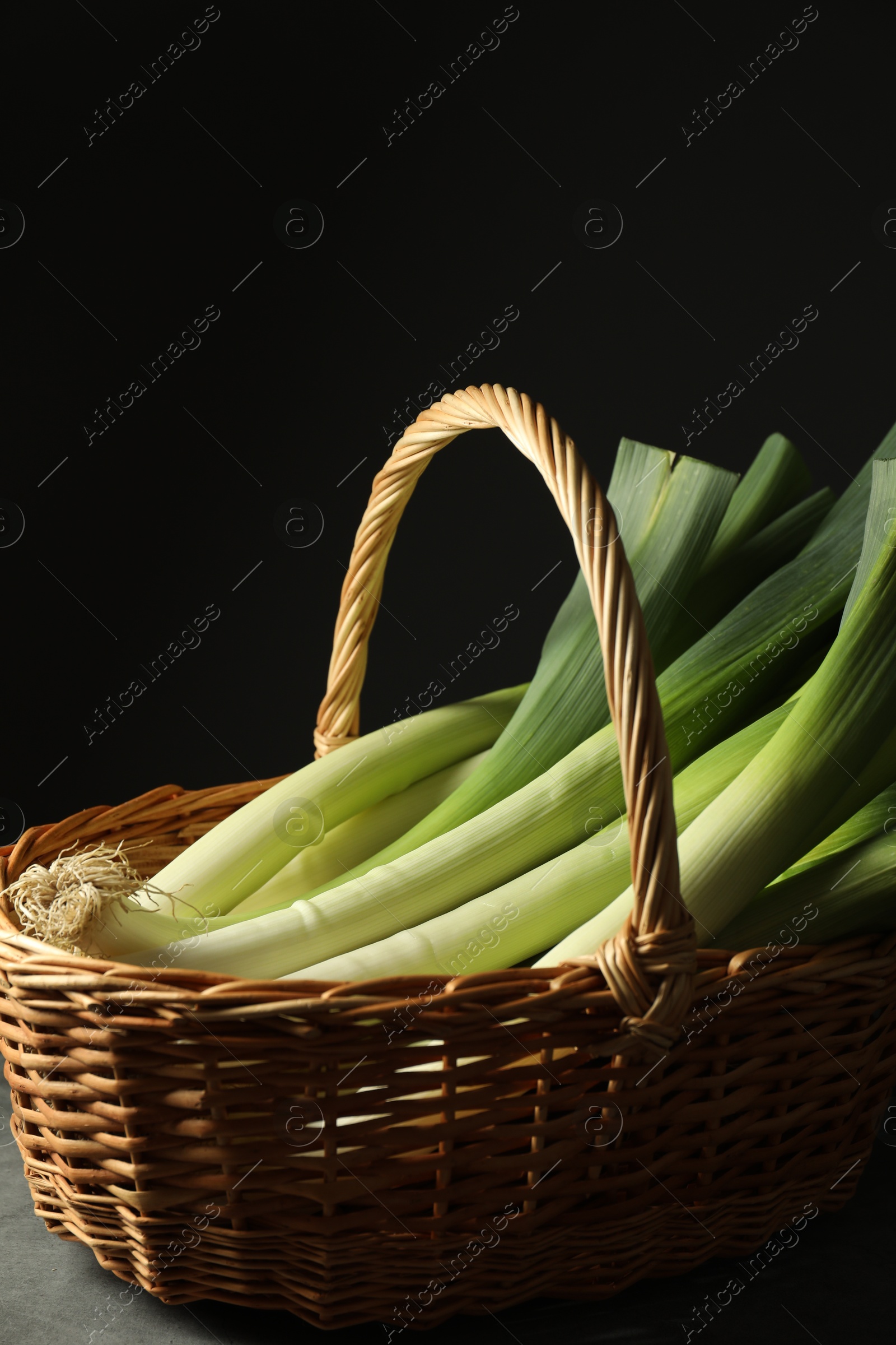 Photo of Fresh leeks in wicker basket on grey table, closeup