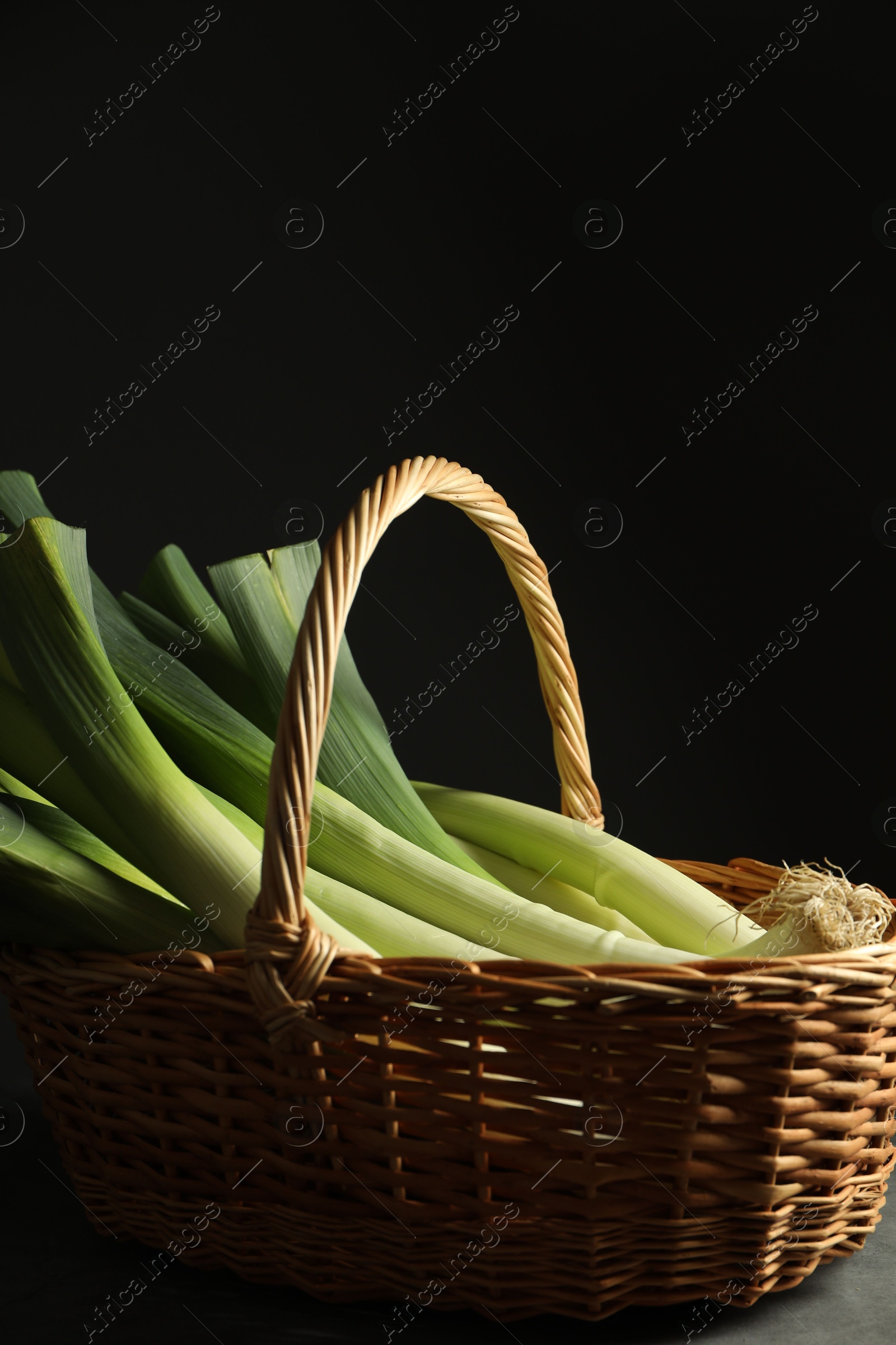 Photo of Fresh leeks in wicker basket on grey table, closeup