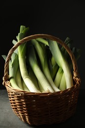 Photo of Fresh leeks in wicker basket on grey table, closeup