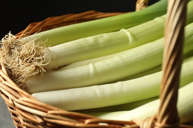 Photo of Fresh leeks in wicker basket on black background, closeup