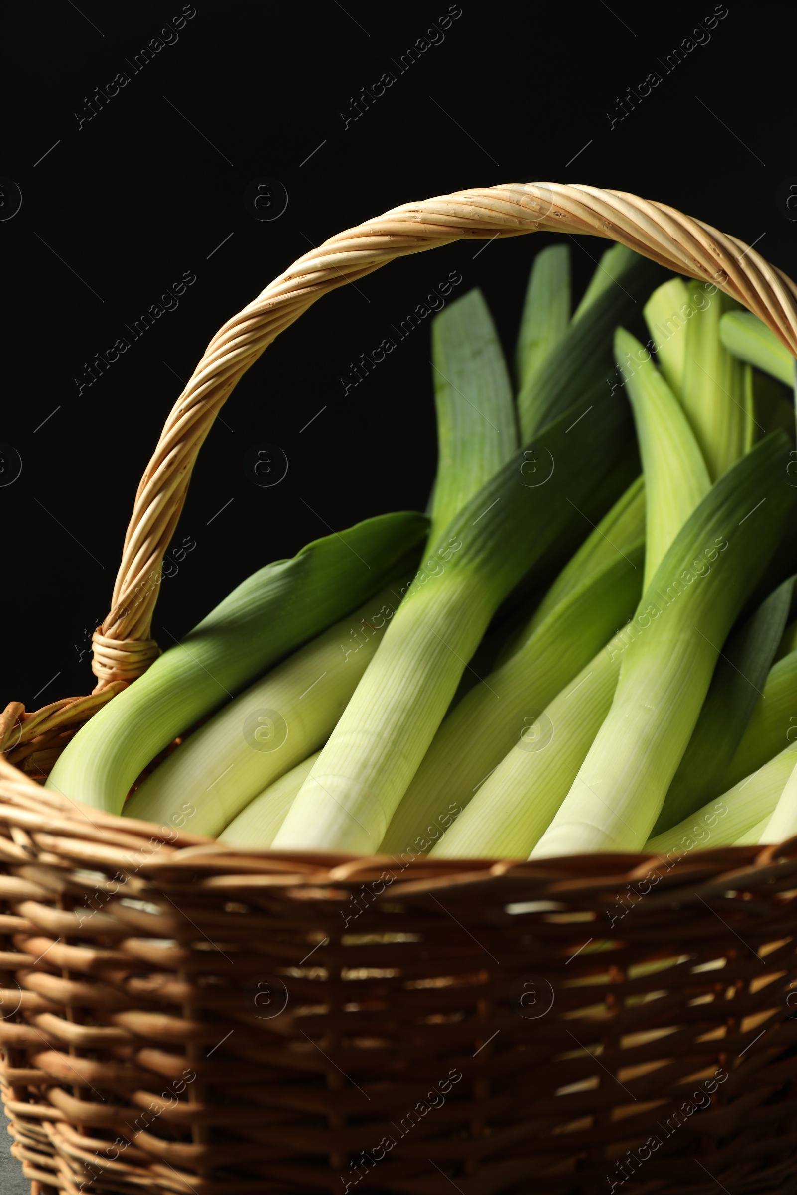 Photo of Fresh leeks in wicker basket on black background, closeup