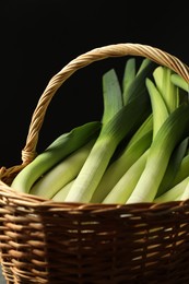 Photo of Fresh leeks in wicker basket on black background, closeup