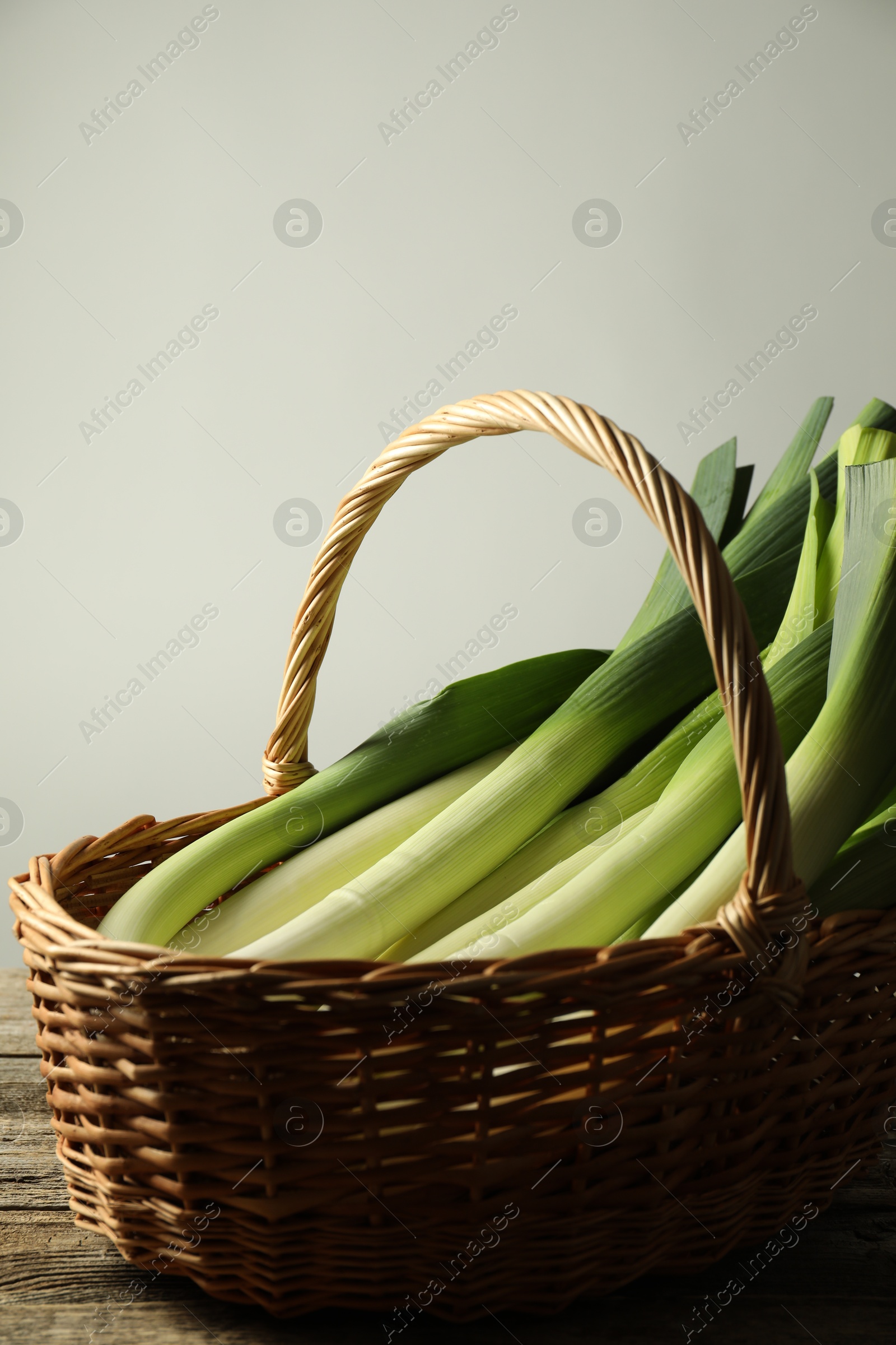 Photo of Fresh leeks in wicker basket on wooden table, closeup