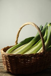 Photo of Fresh leeks in wicker basket on wooden table, closeup