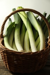 Photo of Fresh leeks in wicker basket on wooden table, closeup