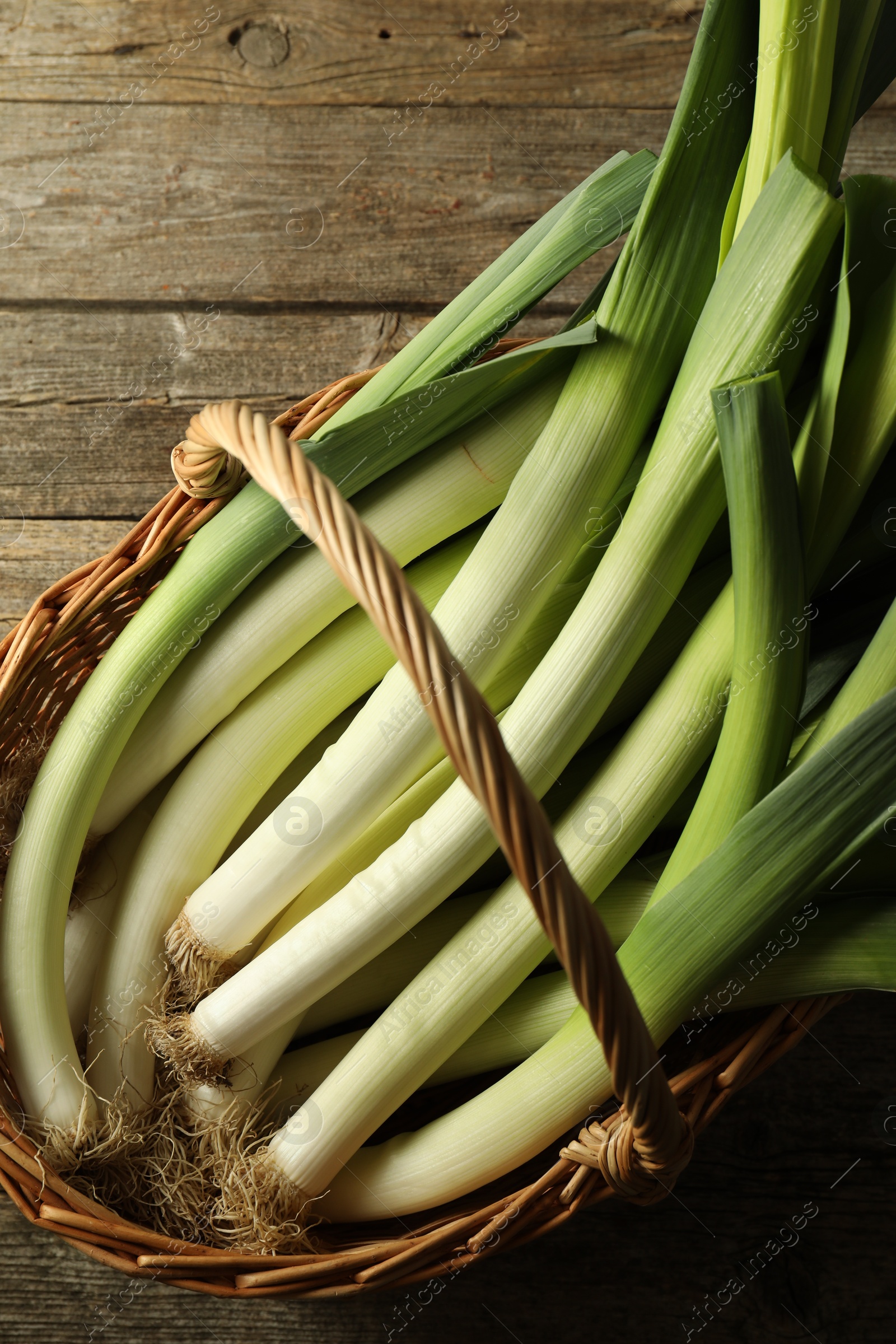 Photo of Fresh leeks in wicker basket on wooden table, top view