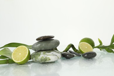 Photo of Spa composition with limes, massage stones and bamboo stem on wet surface against white background